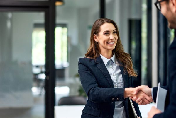 Professional, brunette woman in a modern office setting enthusiastically shakes hands with a professional gentleman