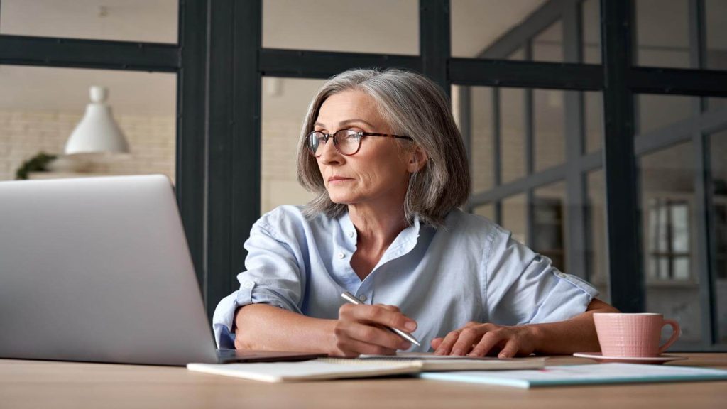 Business woman taking notes while watching laptop sitting at table