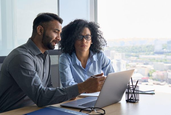 A male and female examine a document on their laptop in a professional office setting